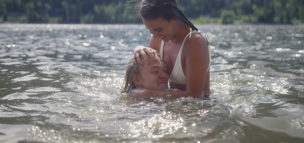 Woman dunks a man's head underwater in a river