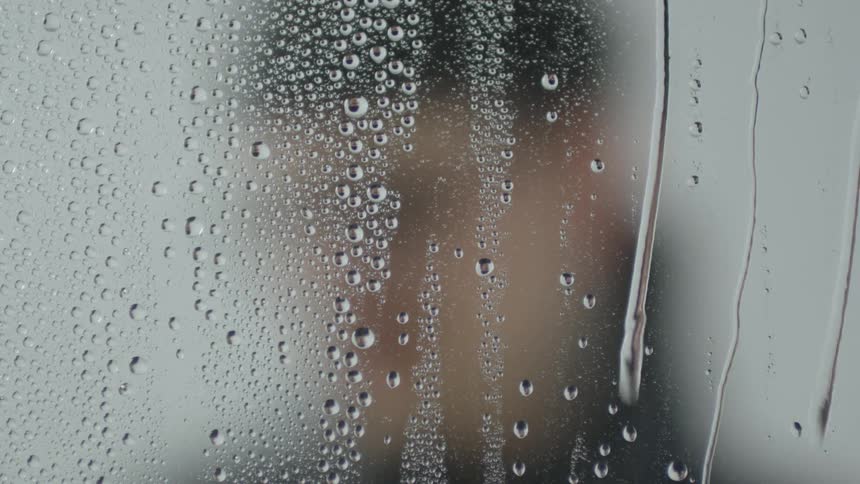 A person stands behind a wet piece of glass