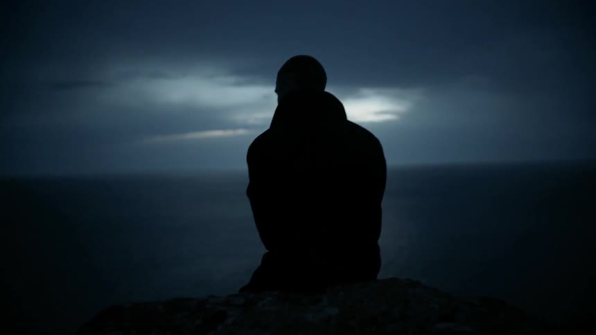 A man sits on the edge of a cliff