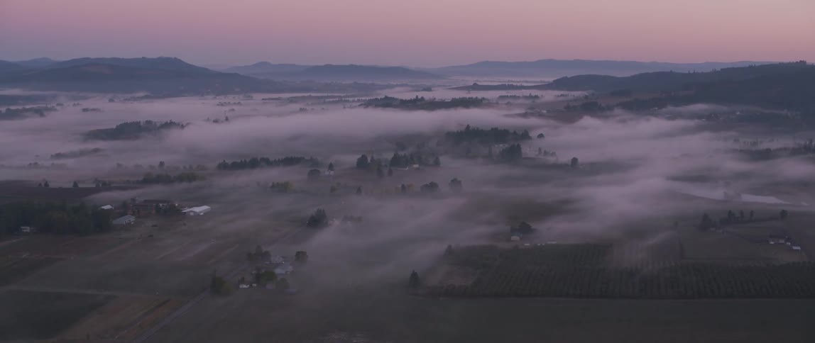 Mist floats over a valley at sunset