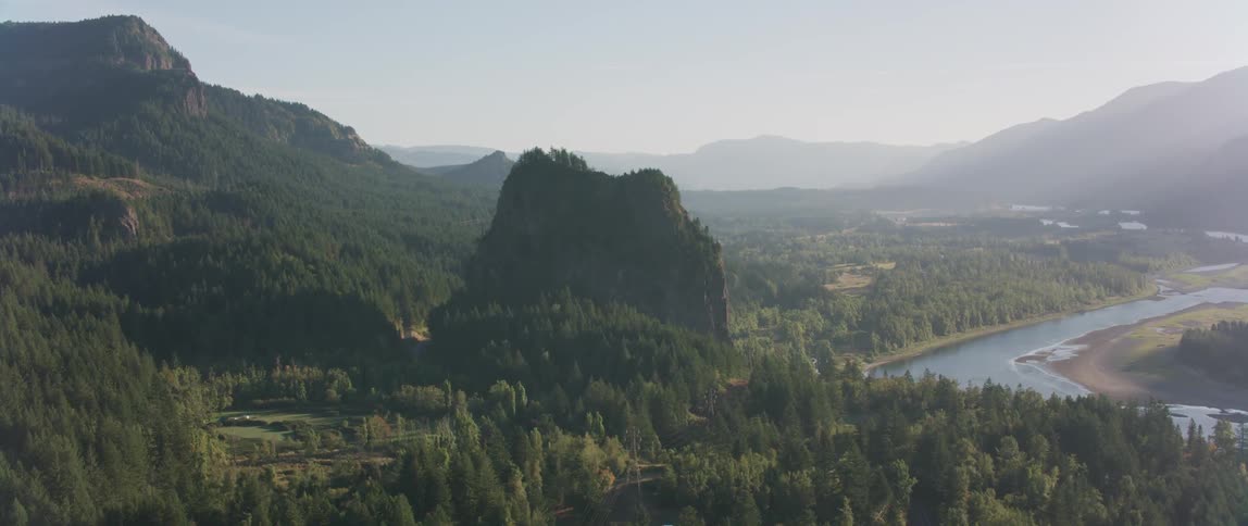A haze is settling over a river in a forested valley during the day