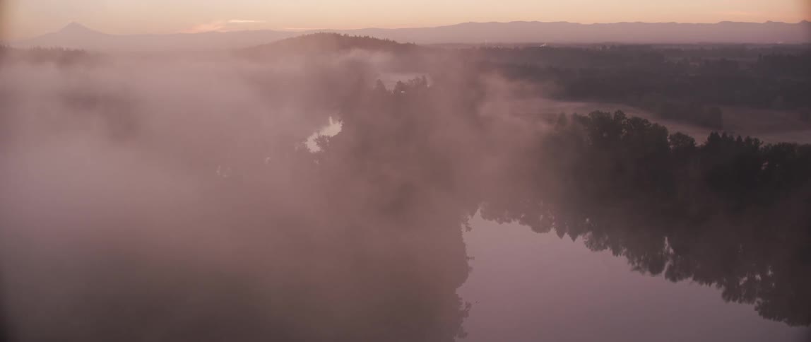 Clouds billow over tree covered hilly land with a river flowing through it