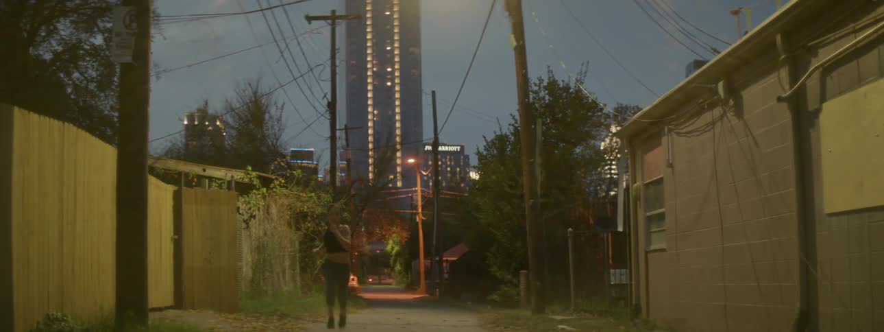 A woman is jogging in a back alley in a city at dusk