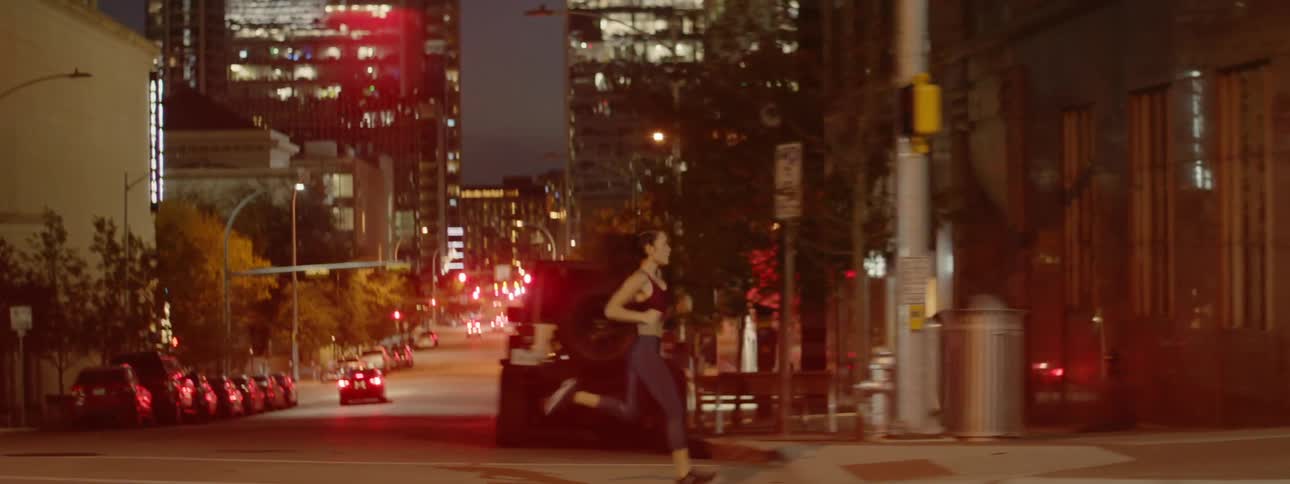 A woman jogs on a city sidewalk at night