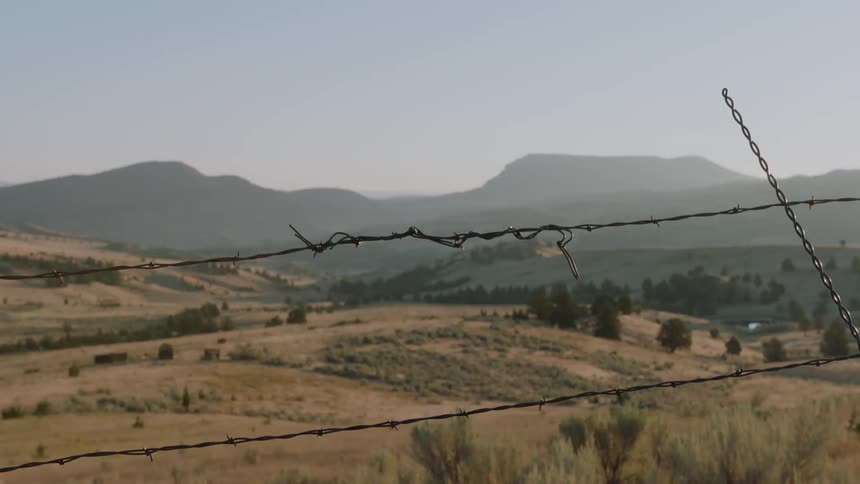 Barbed wire is enclosing a range in a valley on a sunny day