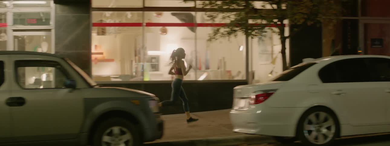 A woman jogs on a city sidewalk at night