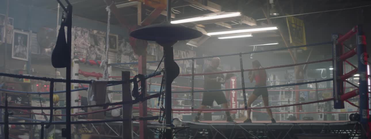 A female fighter is training with a coach inside a boxing ring