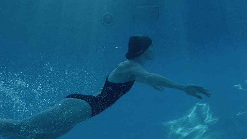 A woman is swimming underwater in a pool during the day