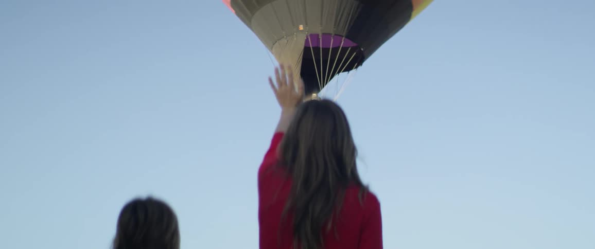 A woman waves as a hot air balloon lifts off