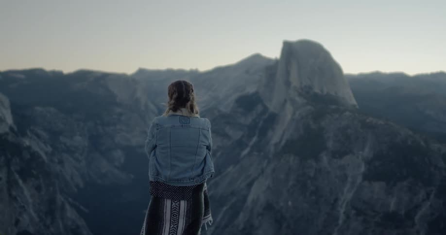 A woman looks out over the steep rocky mountains below