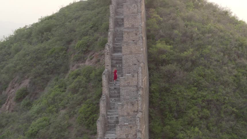A person in red is climbing the steps of a long stone wall going over the mountain
