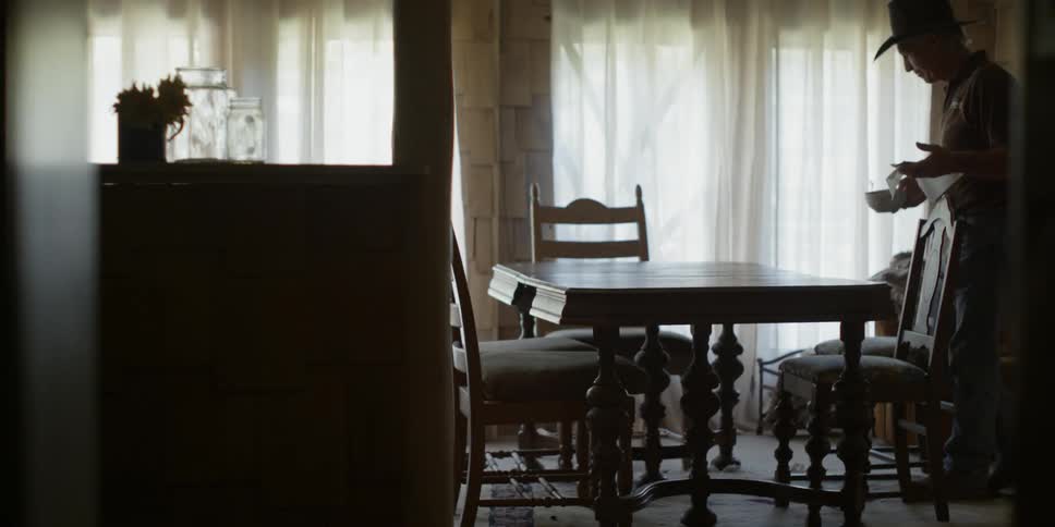 A cowboy sits down at a table to eat from a bowl