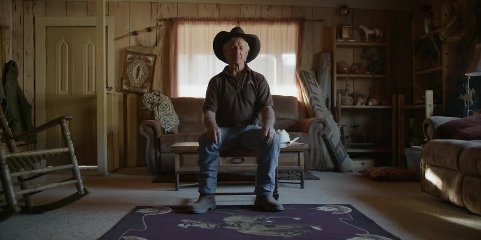 A man sits on a coffee table in a living room