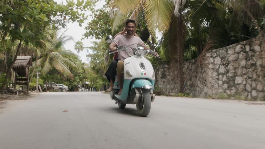 Man and woman ride a motorcycle under the trees