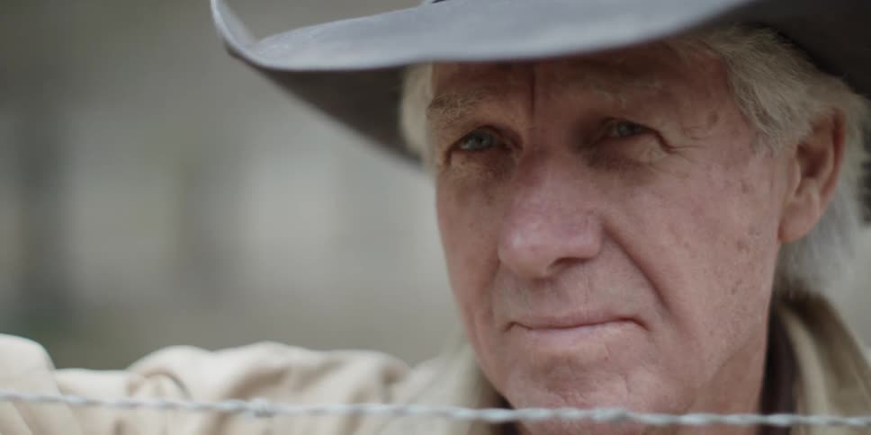 An old man is staring over a barbed wire fence during the day