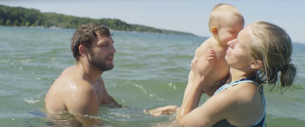 A mom and dad play with their baby in the ocean on a sunny day
