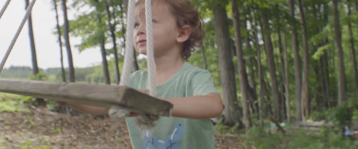 A boy is playing outside pushing a swing
