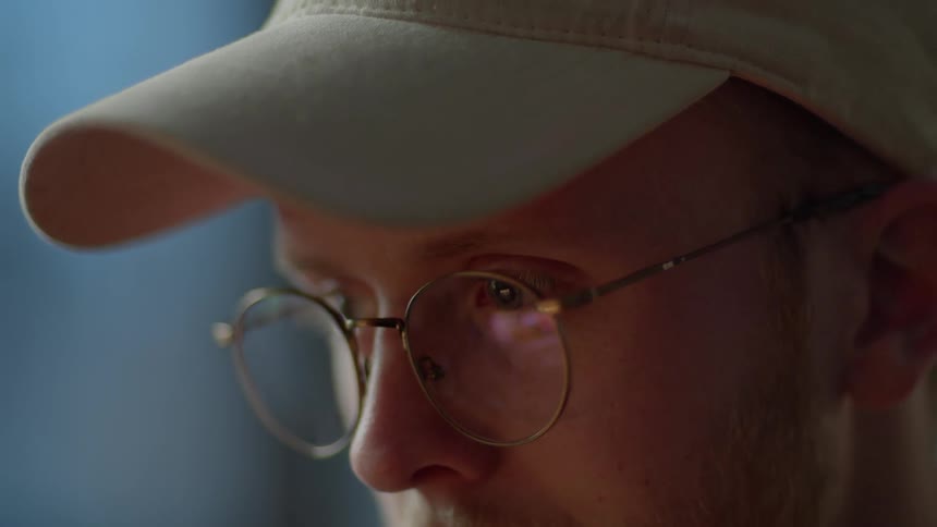 A man with glasses and a hat is looking at something off screen and then bends over