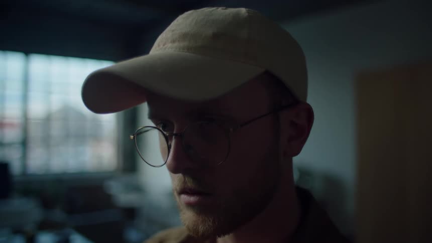 A man with glasses looks forward in the dark room