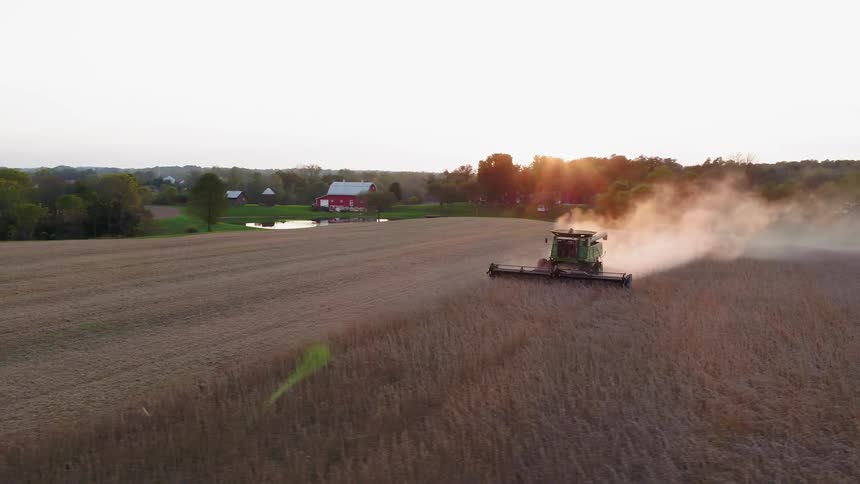 A tractor harvests crops on a farm at sunset