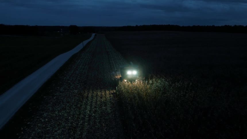 A tractor works the fields moving the crops at night
