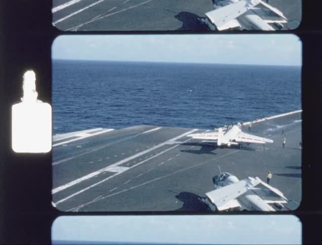 Fighter jets are taxiing on the deck of an aircraft carrier during the day
