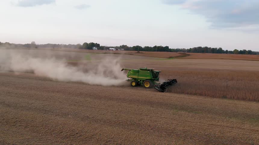 The green tractor slowly moves down the brown farm