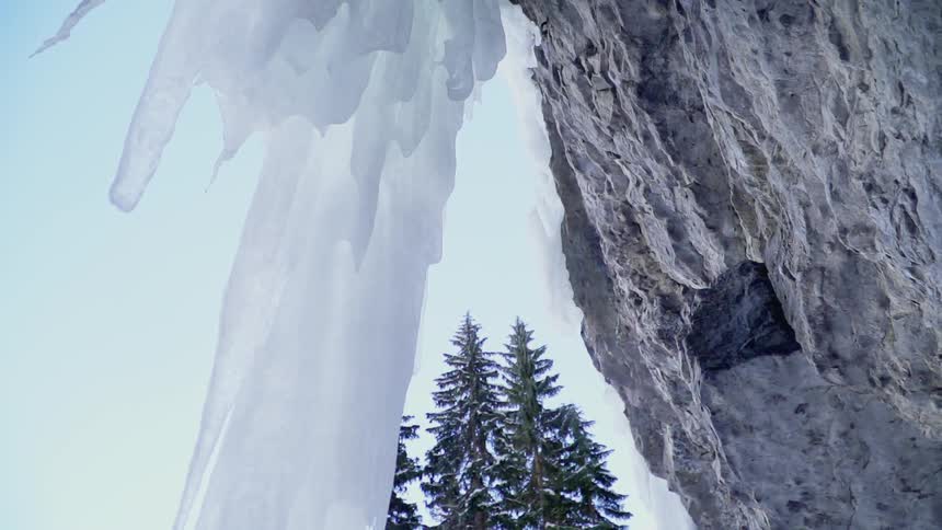 Large icicles hang off a rock formation near trees