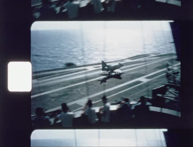 A fighter jet is landing on an aircraft carrier during the day