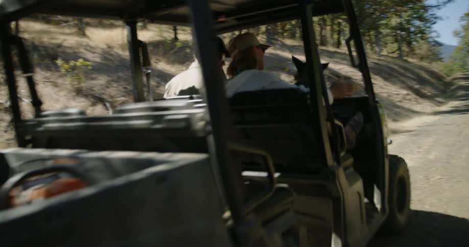 Two people and a dog ride in a small motorized cart through the woods