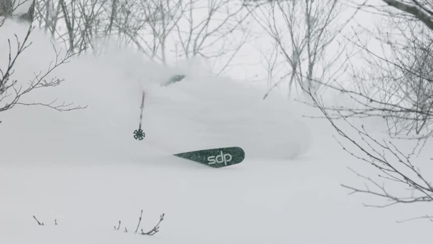 A skier turns through the snow in between trees on a slope