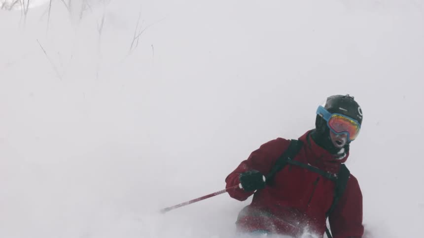 A skier turns through deep snow as he goes down a hillside in daylight