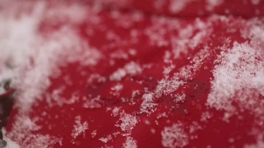 The snow is falling on the red coat and sticking