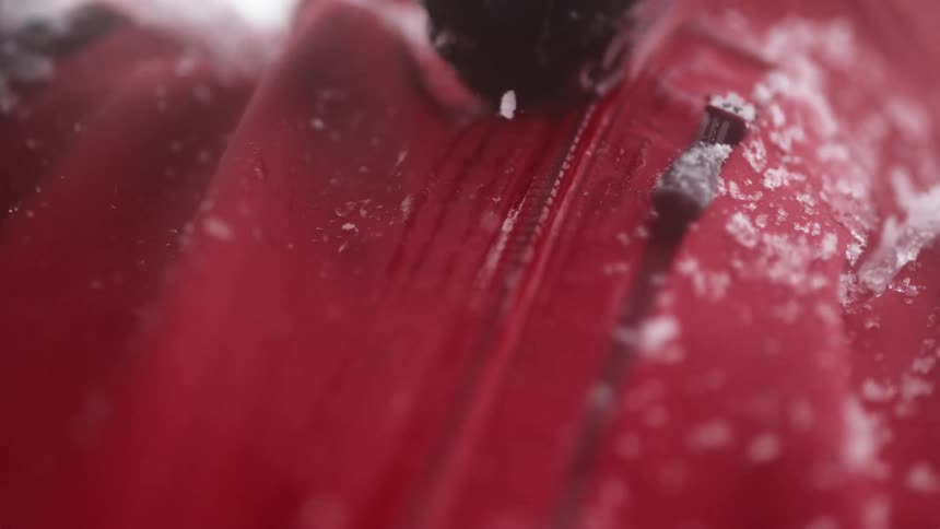A person outside in the snow zips up their red coat