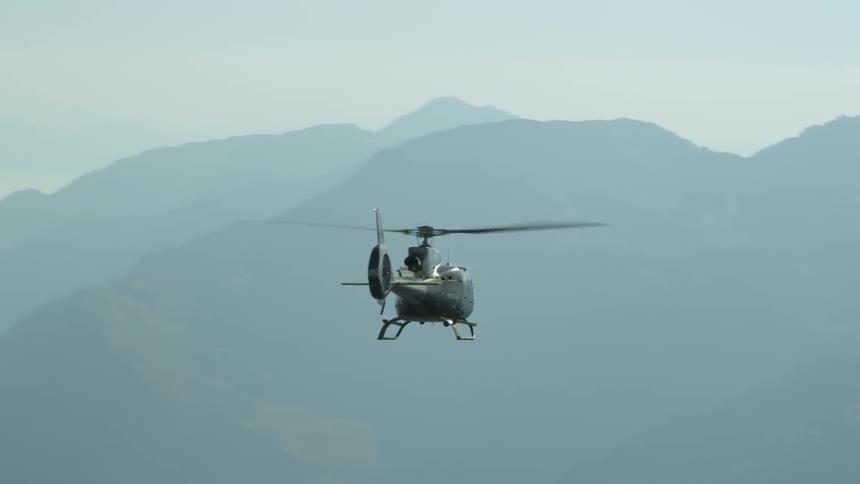 A helicopter is flying above a mountain range in daylight