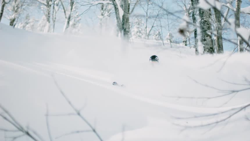 A skier is kicking up snow as he skis downhill during the day