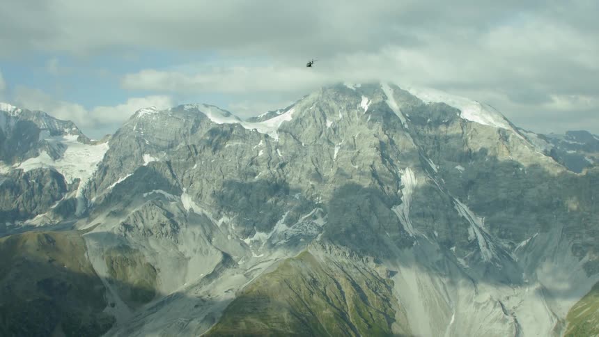 A helicopter moves high over the mountains