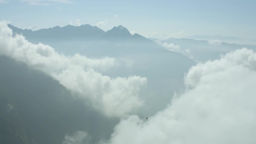 A helicopter flies above white clouds and tall mountains