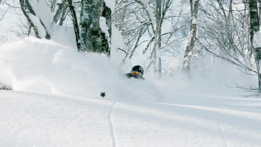 A skier is kicking up deep powder as he skis downhill during the day