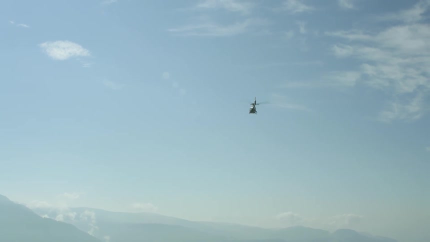 A helicopter flies over mountains on a sunny day
