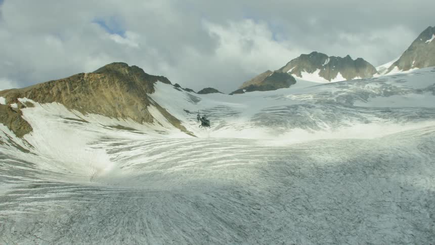 The helicopter flies over the snow covered mountain