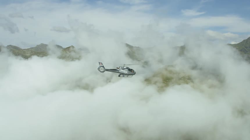 A helicopter flies above the clouds between mountains