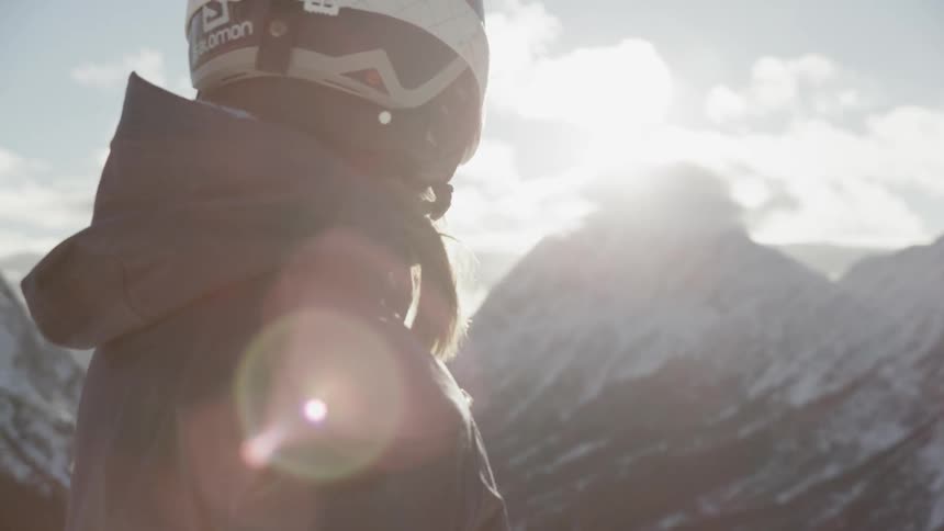 A person with a helmet on looks out over the mountains on a sunny day