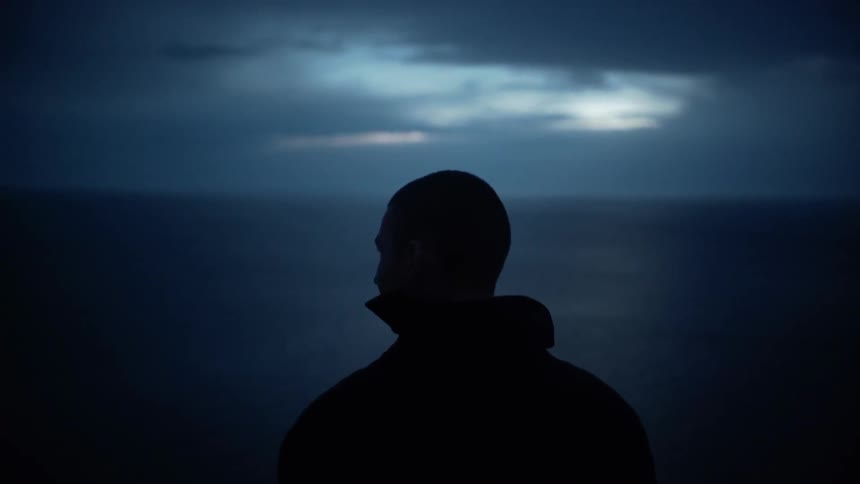 A man looks out onto the water with heavy clouds overhead
