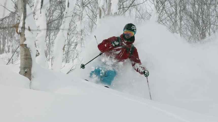 A skier is kicking up deep powder as he skis downhill during the day