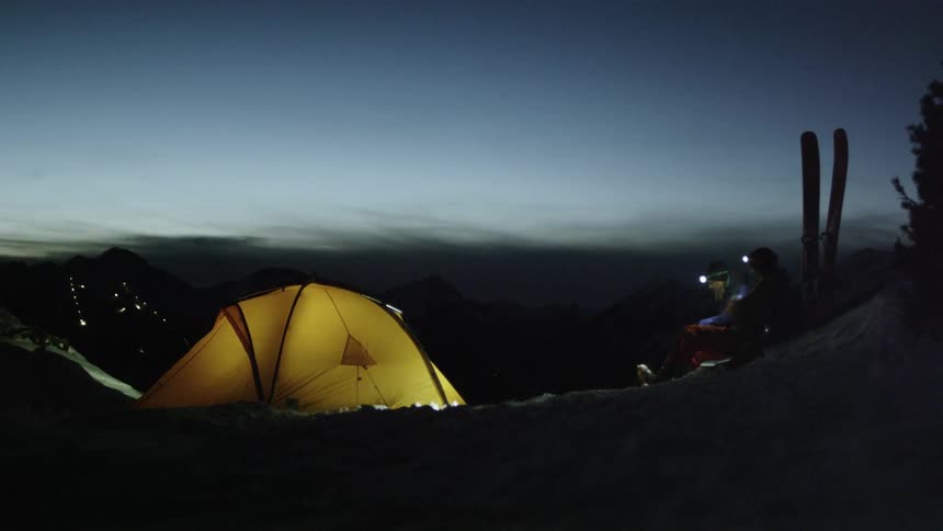Person sitting outdoors next to their small campsite on a clear early evening