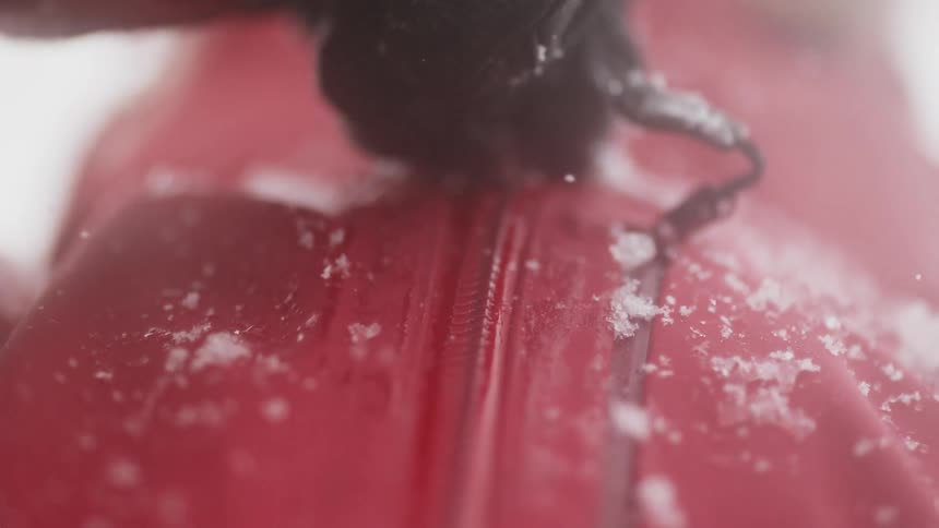 Person zipping up a red jacket that has small pieces of ice on it