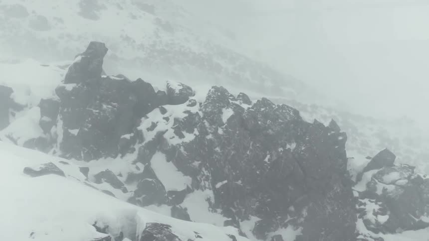 Snow flurries are blowing across a mountainside during the day