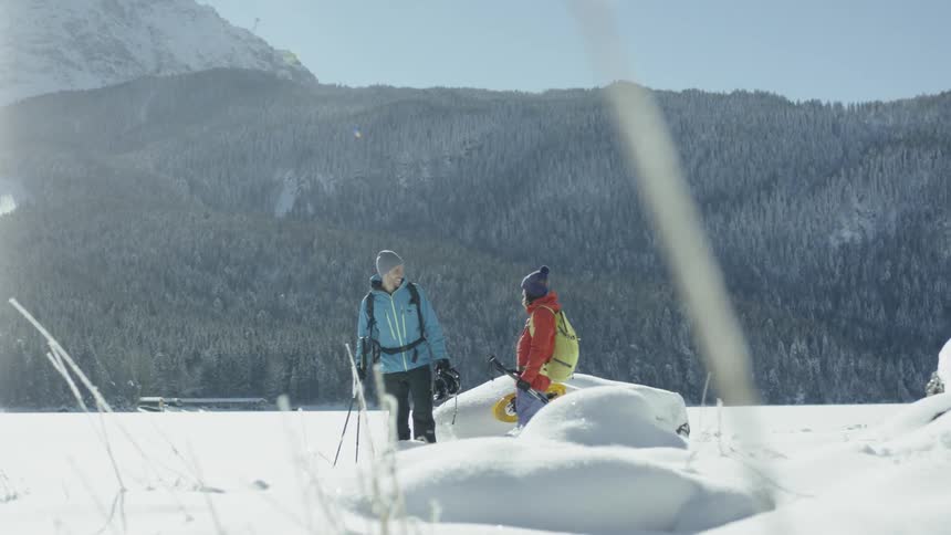 Two skiers talk while standing atop a hill