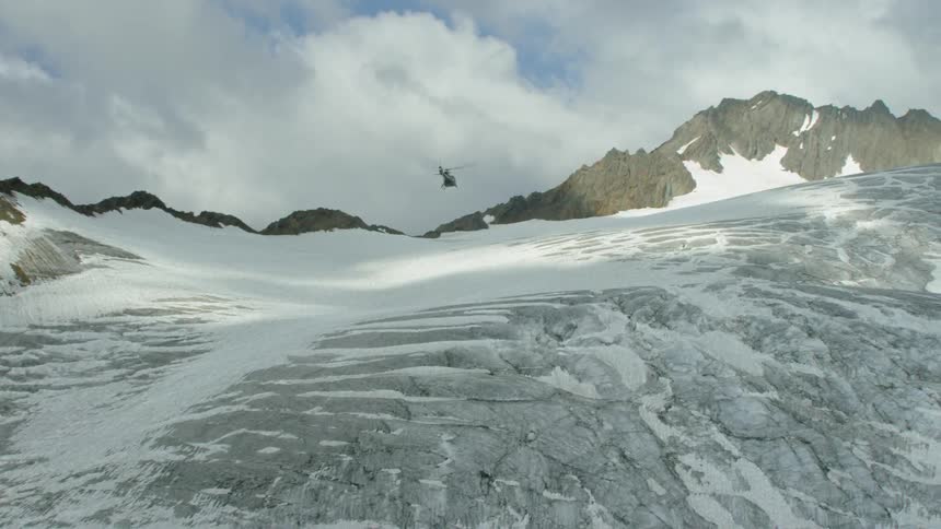 A helicopter flies over an icy and rocky slope